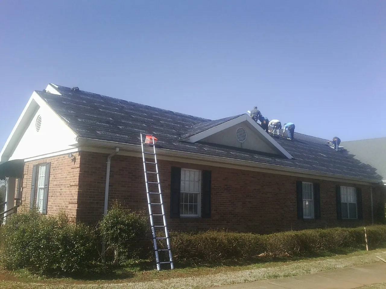 Crew tearing shingles off a brick ranch roof with a ladder set — Emergency Roof Repair work by our crew in Laurys Station