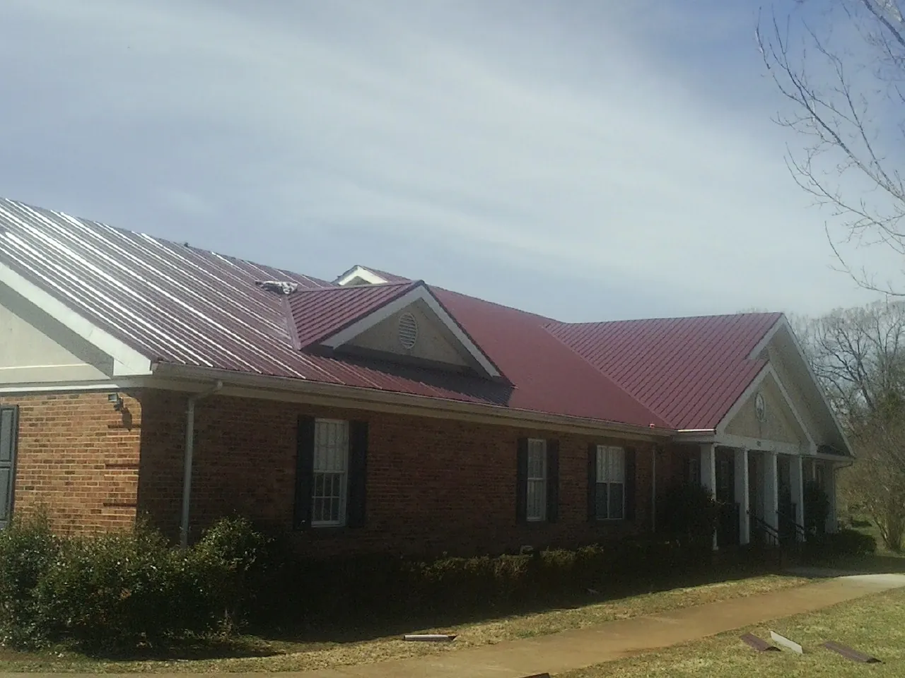 Red metal roof with gabled entries on a long brick building, from a Hail Damage Roof Repair job in Laurys Station