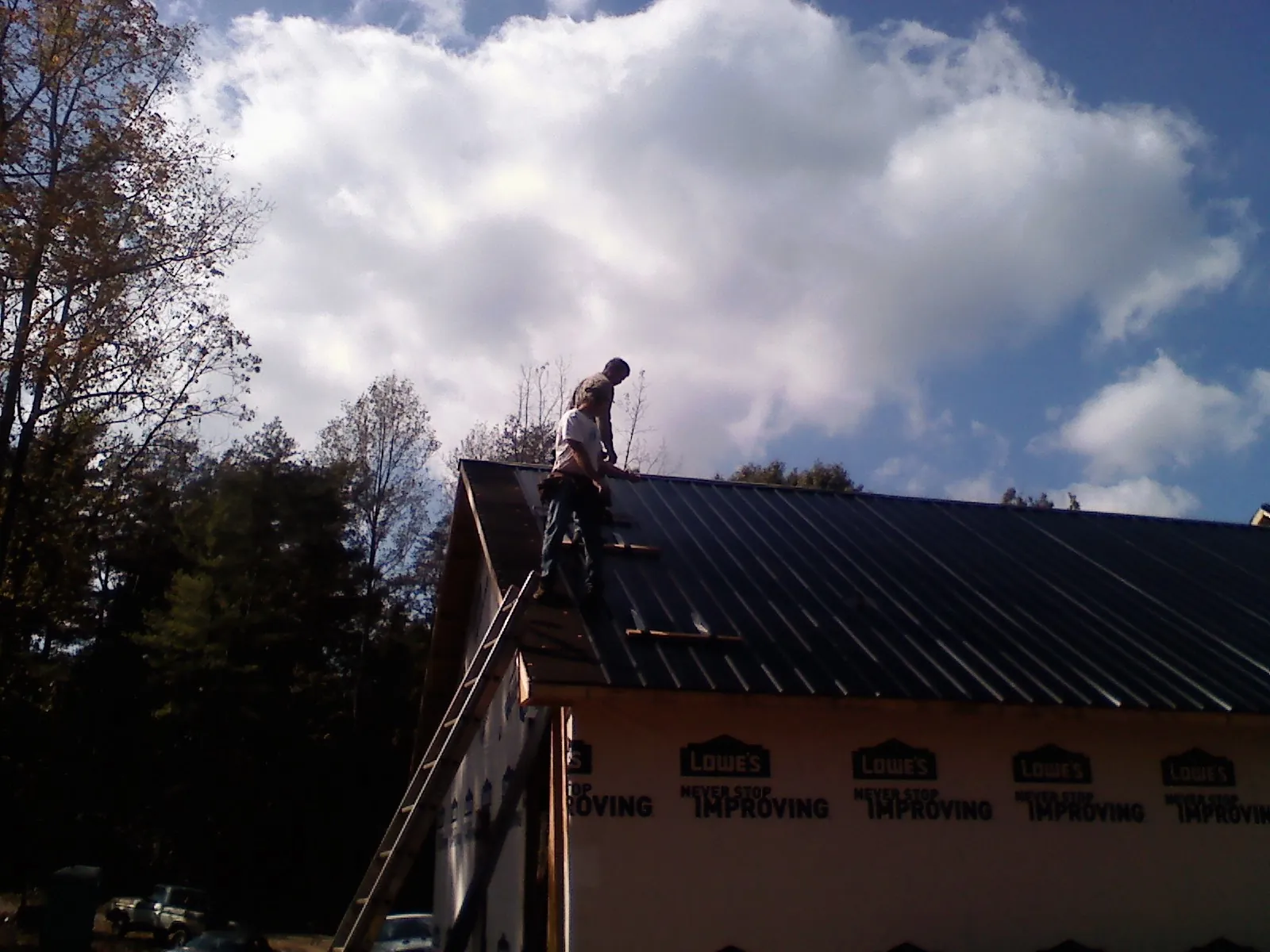 Roofer fastening dark metal panels high against a cloudy sky, from a Roof Inspection job in Laurys Station