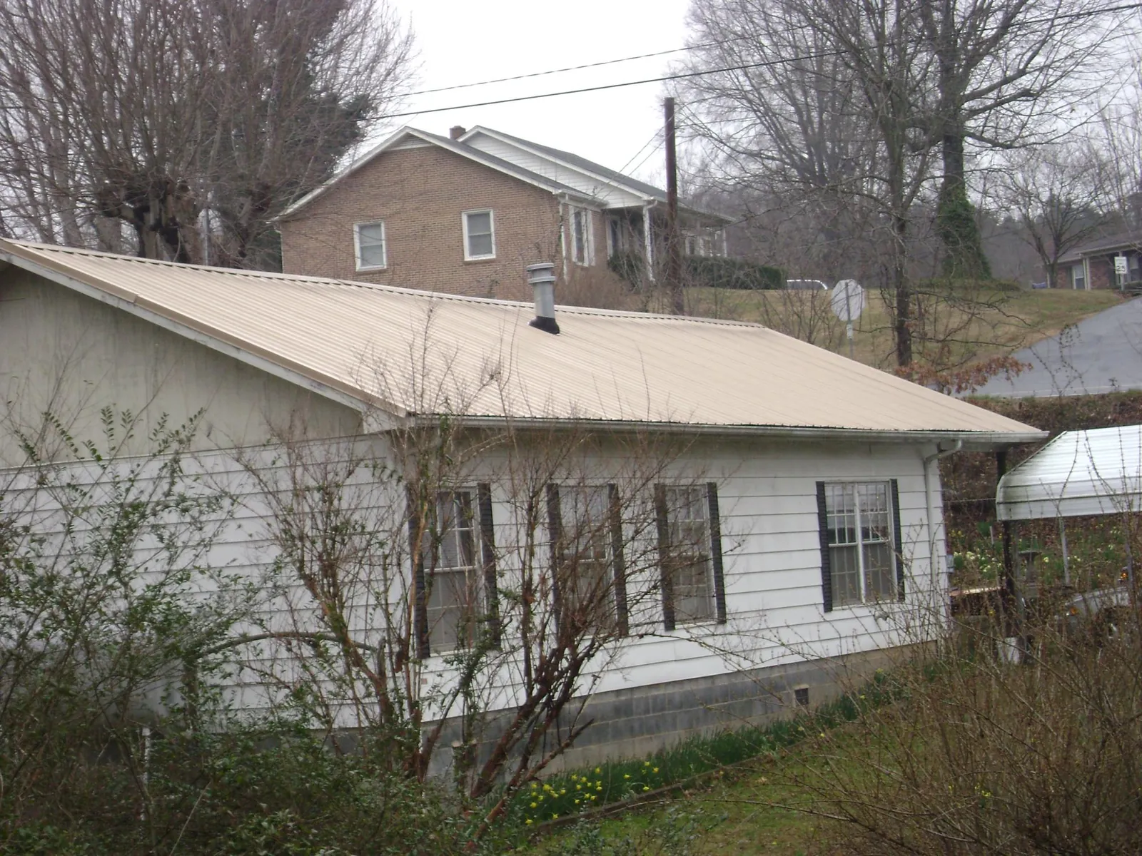 Tan metal roof on a white sided house set into a hillside — Commercial Roofing by Roofing Brothers in Laurys Station